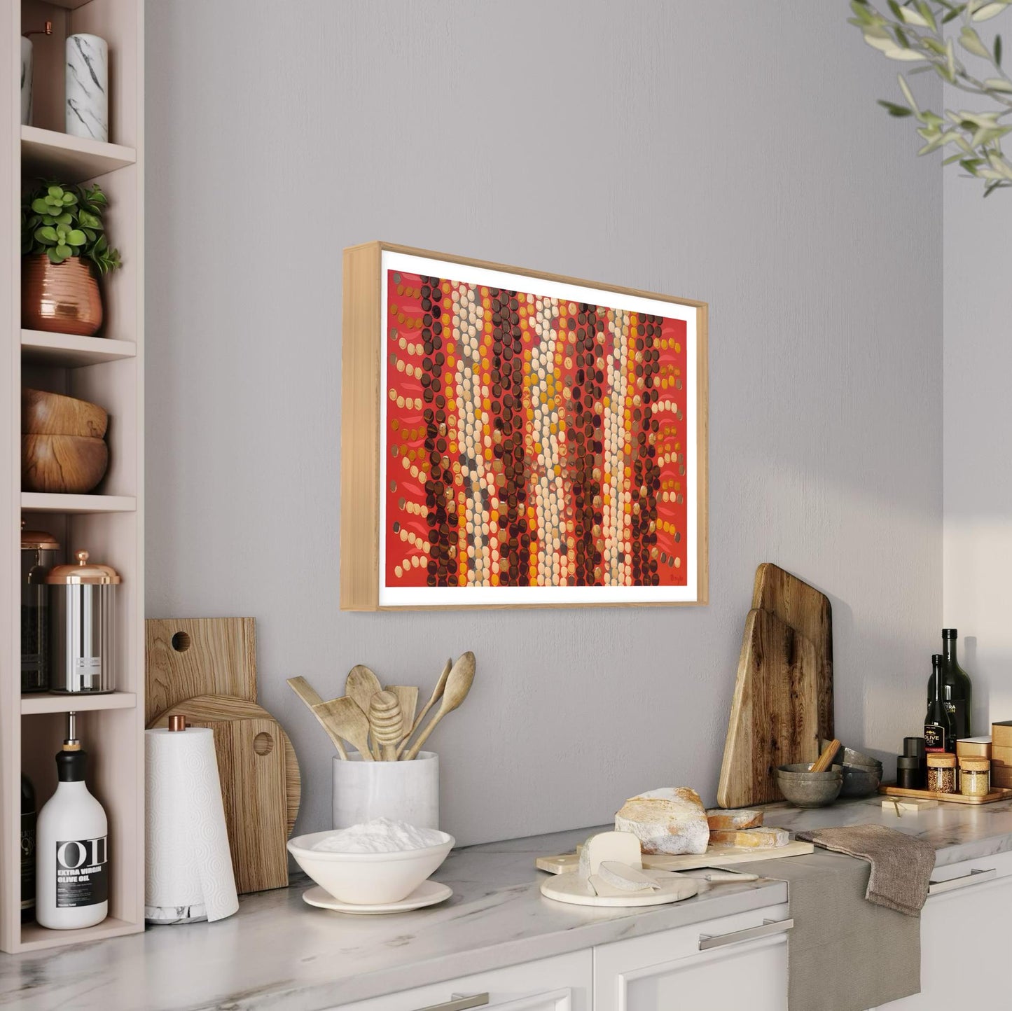 Horizontal Aboriginal dot painting with warm reds, browns, and creams in a light wood frame, styled in a modern kitchen above marble countertops with rustic wooden utensils and breadboards.
