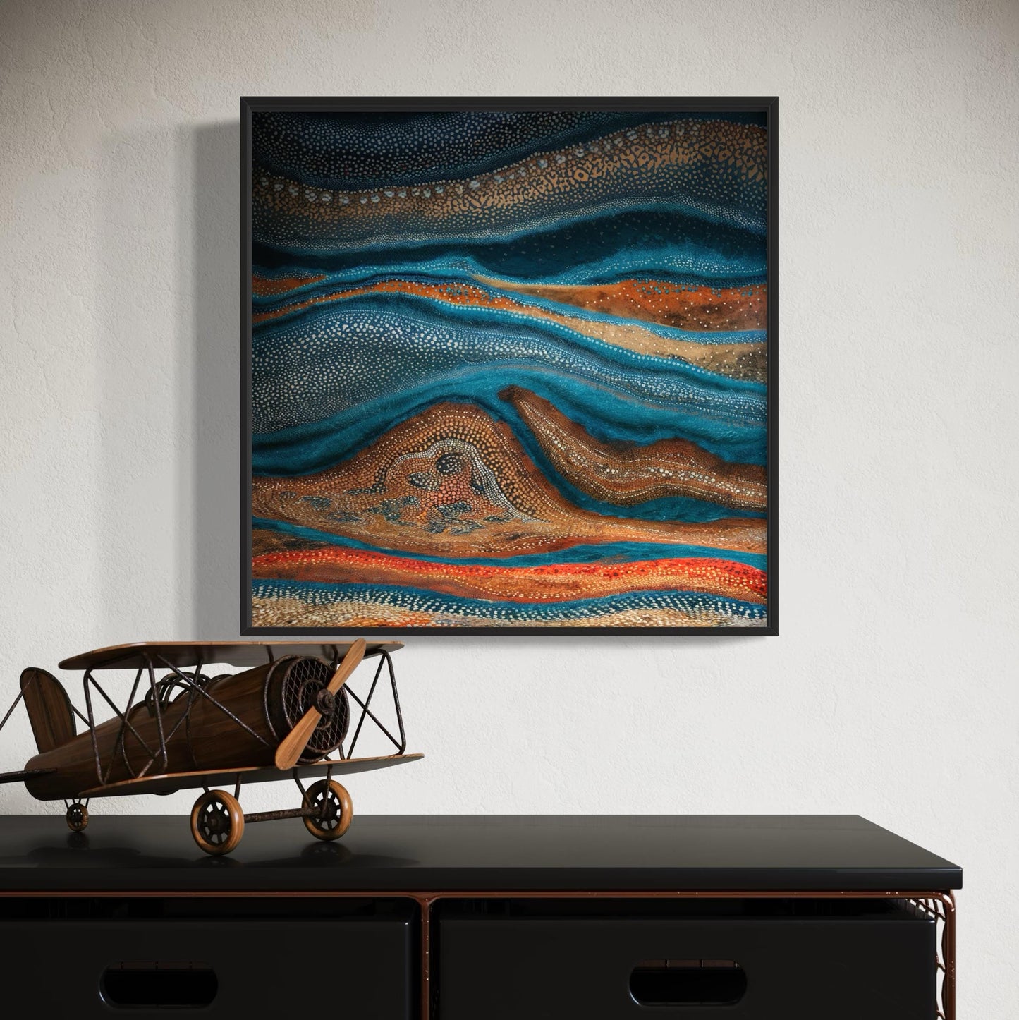 Karli Flow Aboriginal dot painting printable in black frame on white textured wall above dark timber cabinet with decorative wooden airplane model.