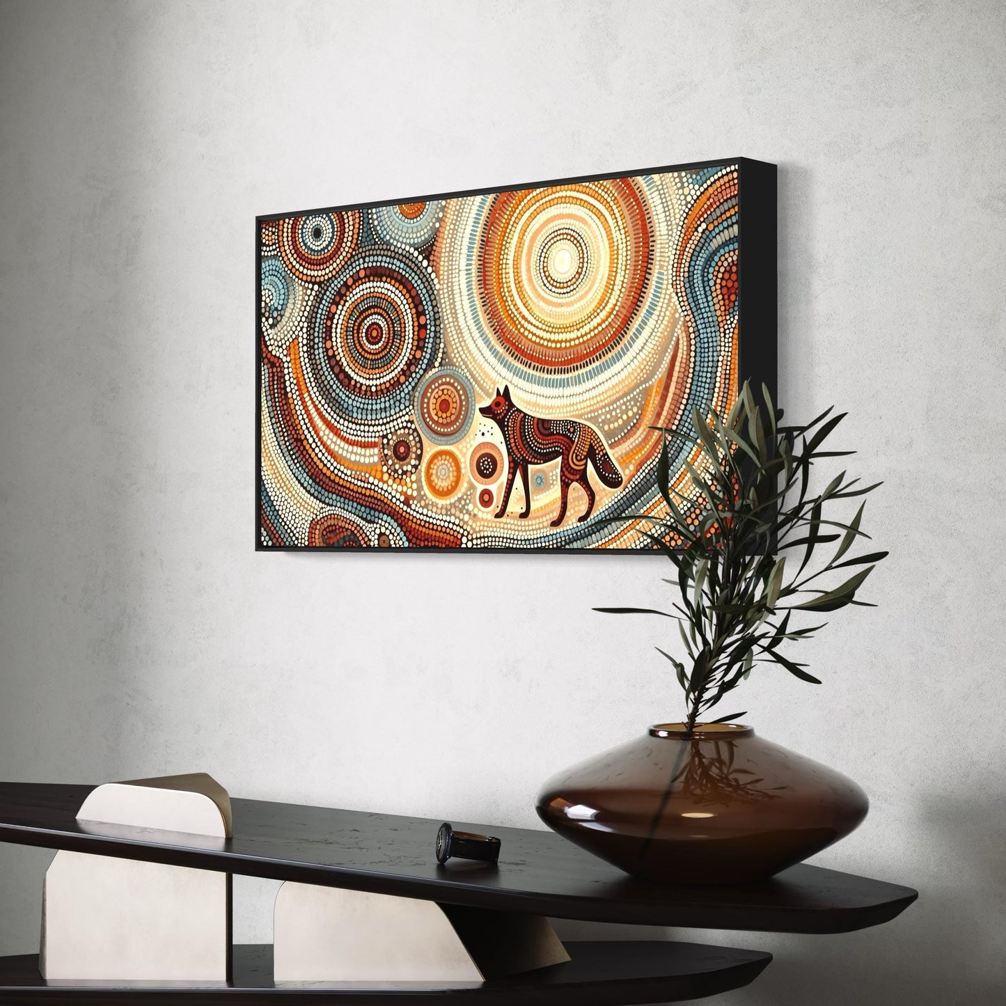 Dharra Dingo Aboriginal dot painting print in ochres and browns, displayed above a black shelf with a vase of olive branches.