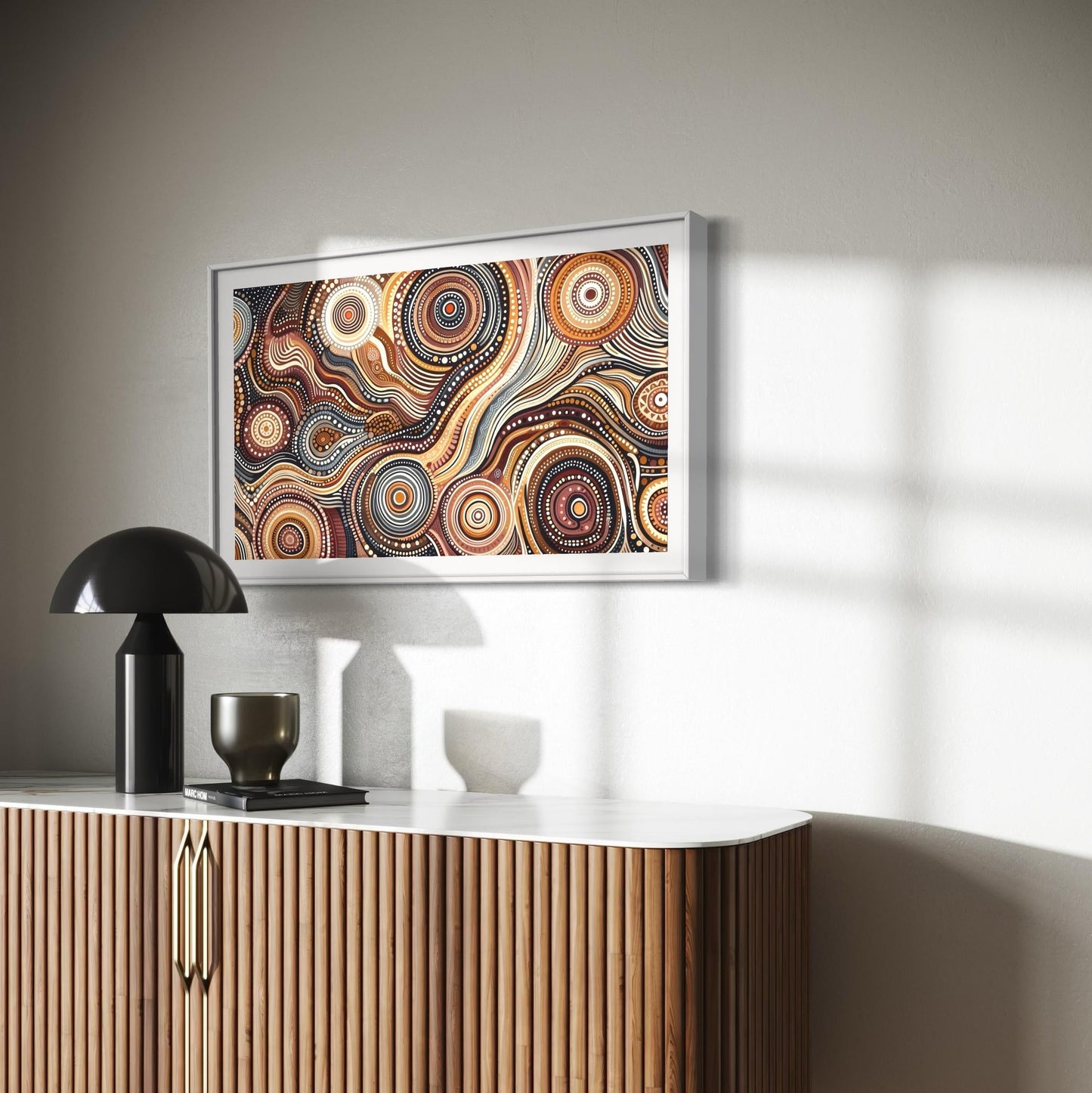 Walu Wirin Aboriginal dot painting horizontal print in white frame above a modern wood and marble console table, styled with a black lamp and ceramic cup, bathed in natural sunlight.