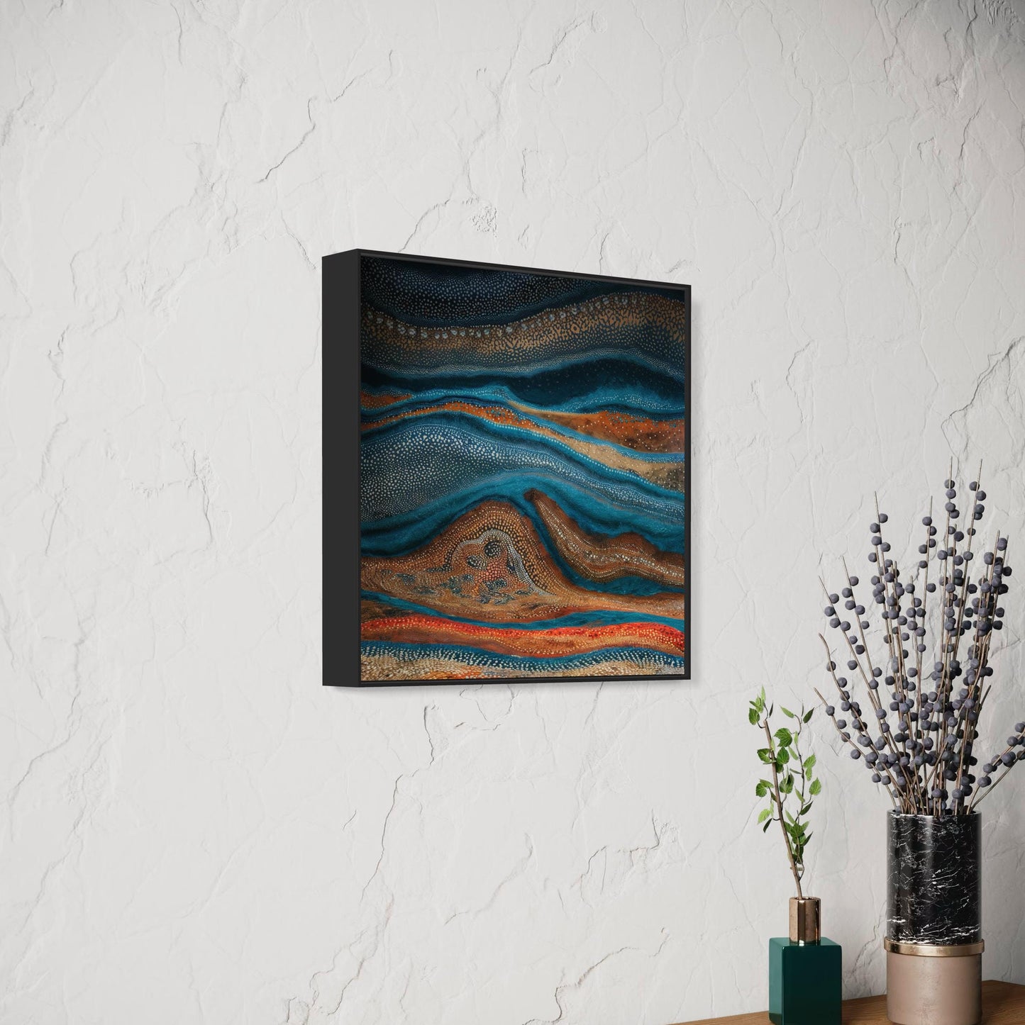 Karli Flow Aboriginal dot painting in a black frame, side view against a textured white wall with decorative vases and foliage, showcasing earthy blues and ochres.