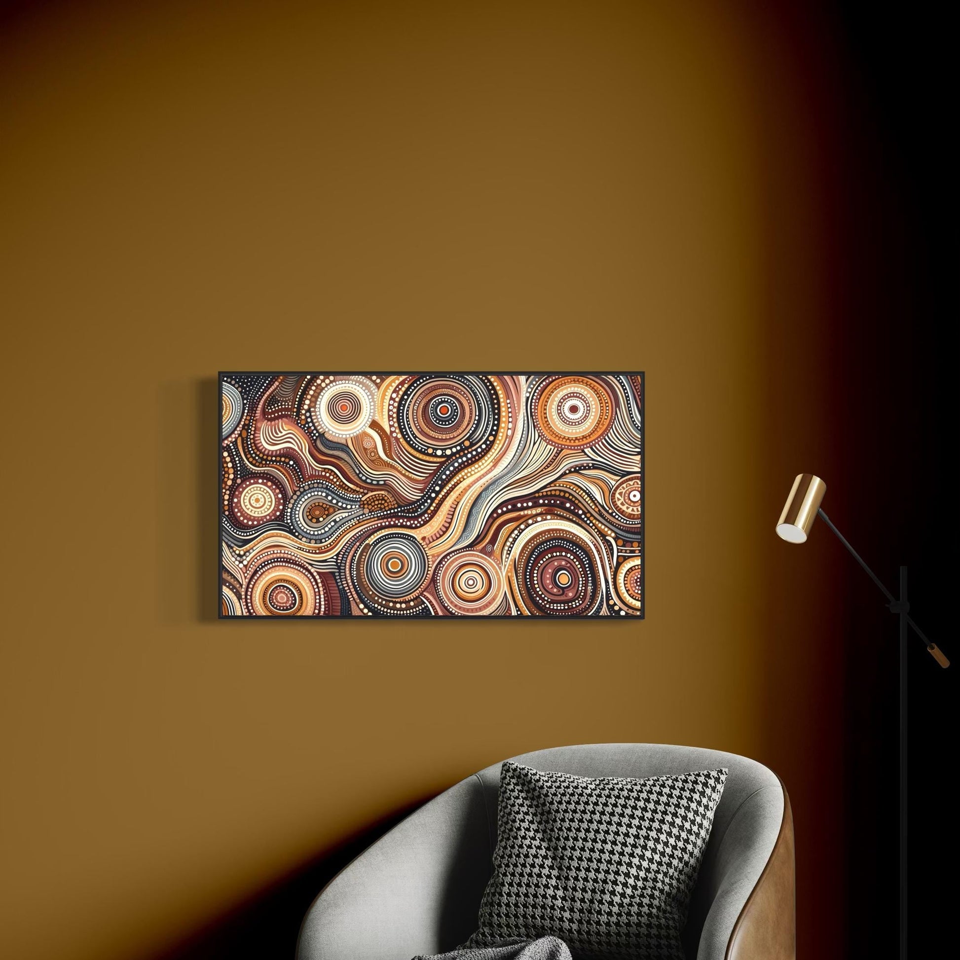 Walu Wirin Aboriginal dot painting horizontal print framed on a warm brown wall above a grey armchair with a houndstooth cushion and grey throw, next to a gold floor lamp.